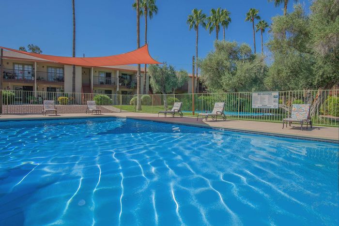 Inviting apartment complex with a sparkling outdoor pool and vibrant palm trees, perfect for relaxation and leisure under sunny skies.