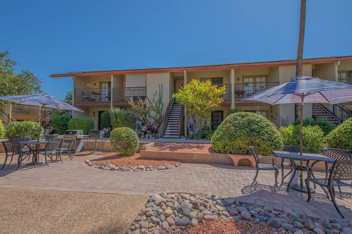Charming apartment exterior with a lush garden, outdoor seating, and sunny blue skies, perfect for relaxation and outdoor dining.