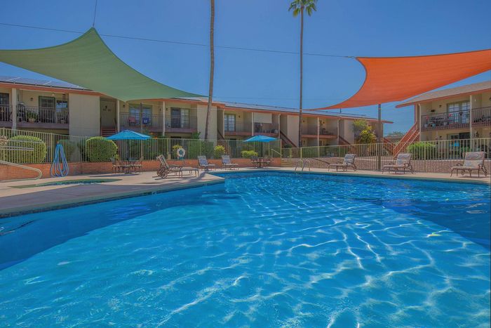 Inviting apartment complex with a crystal-clear swimming pool, sunshade sails, and comfortable lounge chairs for relaxation.