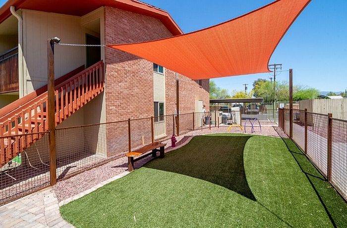 Inviting outdoor area with a sunshade, green lawn, and cozy seating next to a charming brick apartment building.