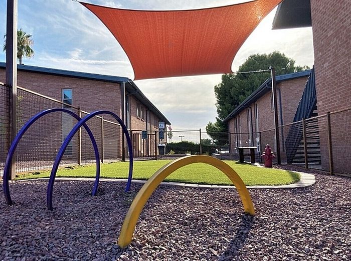Charming apartment courtyard with bright shade sail, colorful playground arches, and vibrant greenery for family enjoyment.