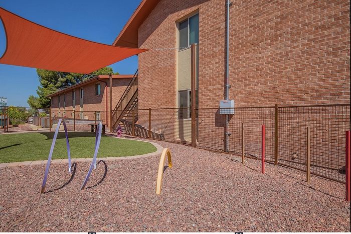 Charming brick apartment exterior featuring a vibrant outdoor play area with bright play structures and lush artificial grass.