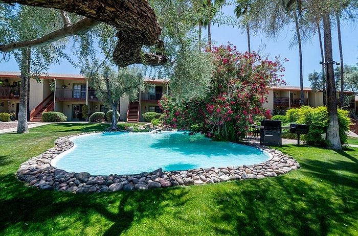 Stunning apartment complex with a crystal-clear pond, surrounded by lush greenery and vibrant flowers, offering a serene outdoor setting.
