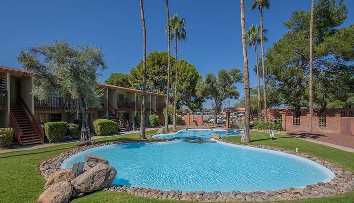 Inviting apartment complex with a sparkling pool surrounded by lush greenery and tall palm trees, offering a serene outdoor oasis.