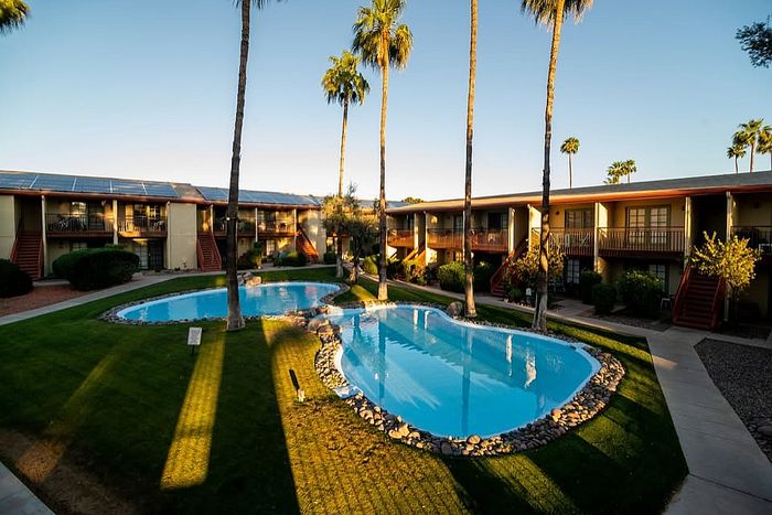 Charming apartment complex with a sparkling pool surrounded by lush greenery and tall palm trees, offering serene outdoor living spaces.