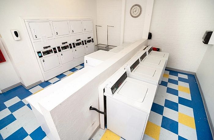 Modern laundry room with multiple washers and dryers, featuring vibrant blue and yellow checkered floor tiles and a wall clock.