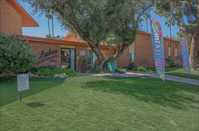 Inviting apartment entrance with well-maintained landscaping, colorful banners, and lush greenery.