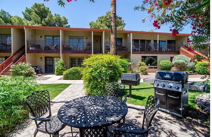 Charming apartment complex with lush greenery, outdoor seating, and a barbecue area, offering a serene community atmosphere.