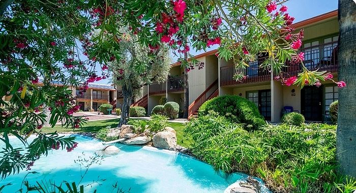 Charming apartment complex surrounded by lush gardens and a serene pond, showcasing vibrant flowers and greenery.