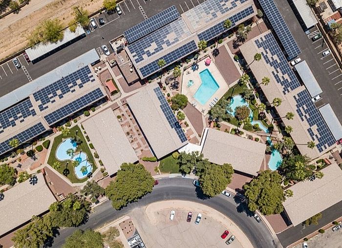 Aerial view of a vibrant apartment complex with solar panel rooftops and refreshing pools, surrounded by lush greenery and scenic pathways.