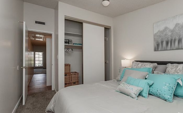 Inviting bedroom featuring a cozy bed, teal accents, and a spacious closet in a serene apartment setting.