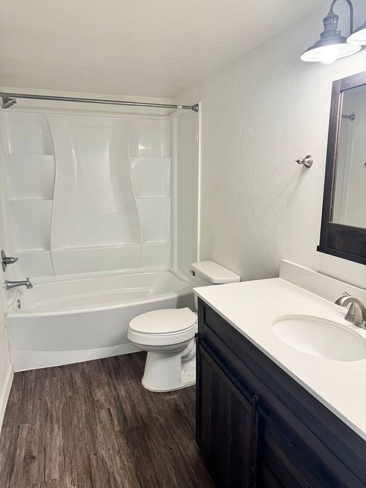 Modern bathroom featuring sleek white fixtures, elegant wood flooring, and stylish light fixtures.