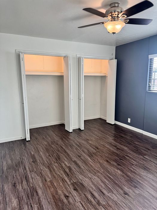 Modern bedroom with sleek wood flooring, double closets, and a ceiling fan for optimal comfort and style.