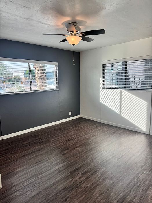 Bright and modern room with sleek dark wood flooring, large windows, and a stylish ceiling fan.