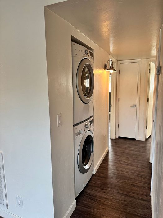 Modern apartment hallway featuring an elegant stacked washer and dryer against warm-toned walls, complemented by rich wooden flooring.