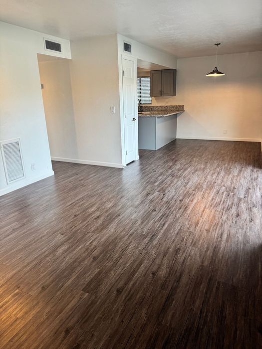 Modern open-concept living space with rich wood flooring and a sleek kitchen, offering ample natural light and contemporary design.