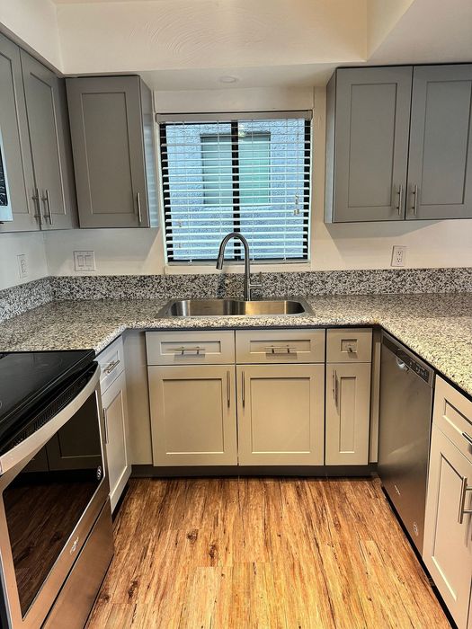 Modern kitchen with stylish gray cabinets, granite countertops, stainless steel appliances, and elegant wood flooring.