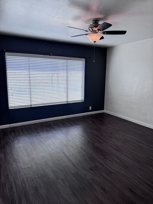 Modern room with sleek dark wooden flooring, a stylish ceiling fan, and large window for natural light.