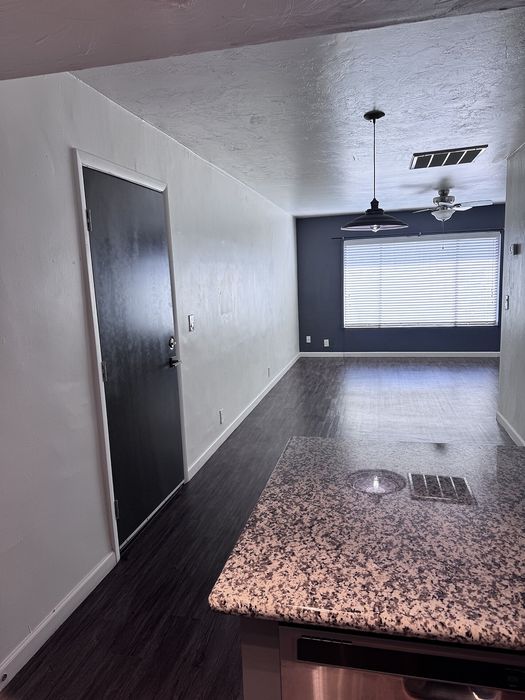 Modern apartment interior featuring a sleek granite countertop, dark wood floors, and ample natural light through large windows.