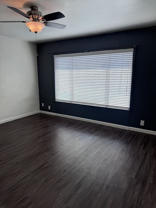 Inviting room with elegant dark wood flooring, large bright window, and modern ceiling fan, perfect for customizable living space.