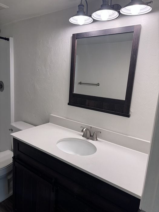 Modern bathroom with elegant dark wood vanity, sleek countertop, and stylish lighting fixtures.