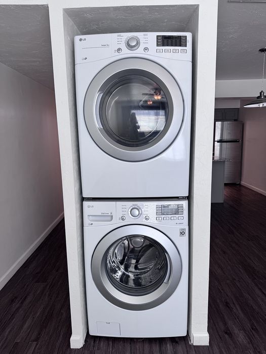 Modern apartment featuring a convenient in-unit stacked washer and dryer set, complemented by sleek dark wood flooring.