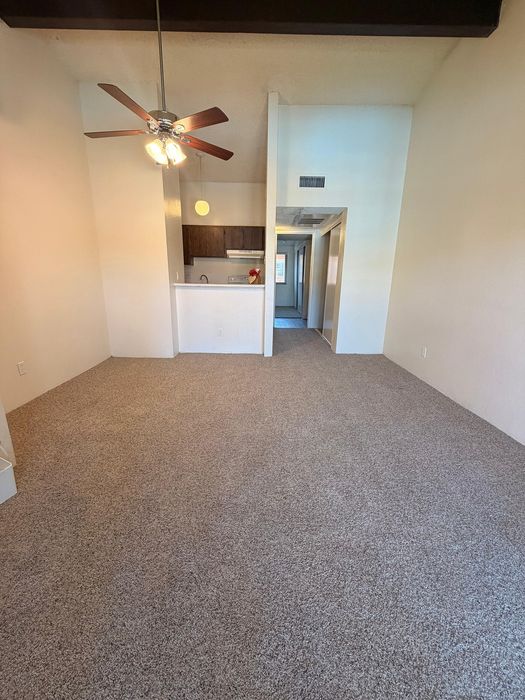 Inviting apartment interior with plush carpet, ceiling fan, and a cozy kitchen nook.