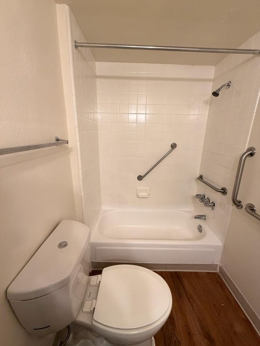 Inviting bathroom featuring a pristine white bathtub with sleek grab bars, complemented by an elegant toilet and modern fixtures, showcasing a blend of comfort and accessibility.
