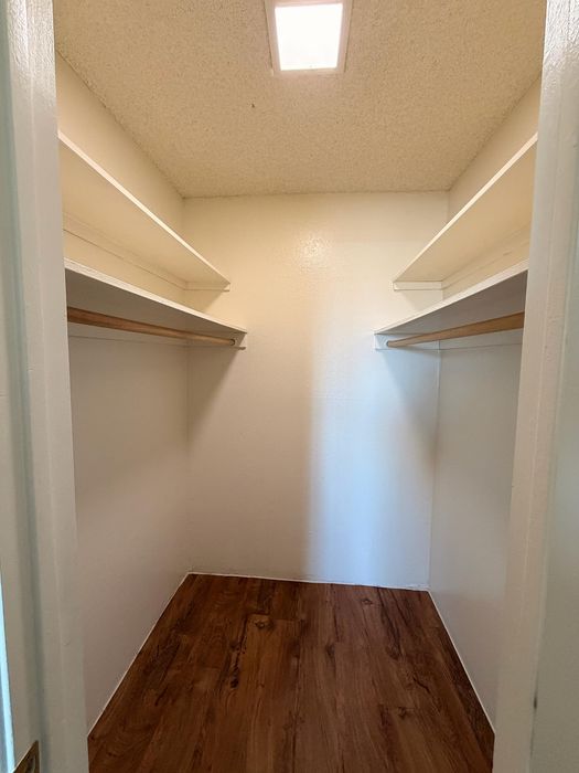 Spacious walk-in closet with elegant wooden flooring and ample shelving, perfect for organized living.