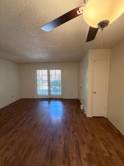 Inviting living area with polished hardwood floors, natural light through large windows, and modern ceiling fan.