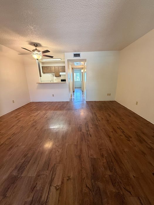 Spacious living area with elegant wooden flooring and open kitchen layout, featuring a modern ceiling fan and ample natural light.