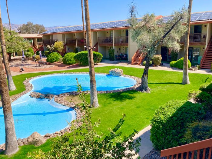 Charming apartment complex with a vibrant landscaped courtyard featuring a sparkling pool and lush greenery.