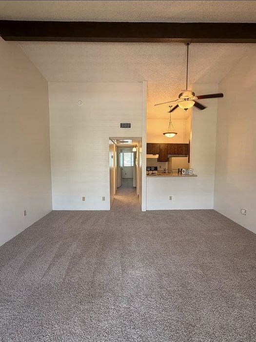 Inviting open-plan living area with plush carpet, ceiling fan, and cozy kitchen nook, ideal for comfortable and stylish living.