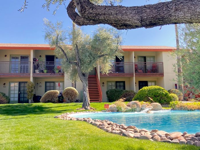 Charming apartment complex featuring lush landscaping, a sparkling pool, and inviting balconies under a clear blue sky.