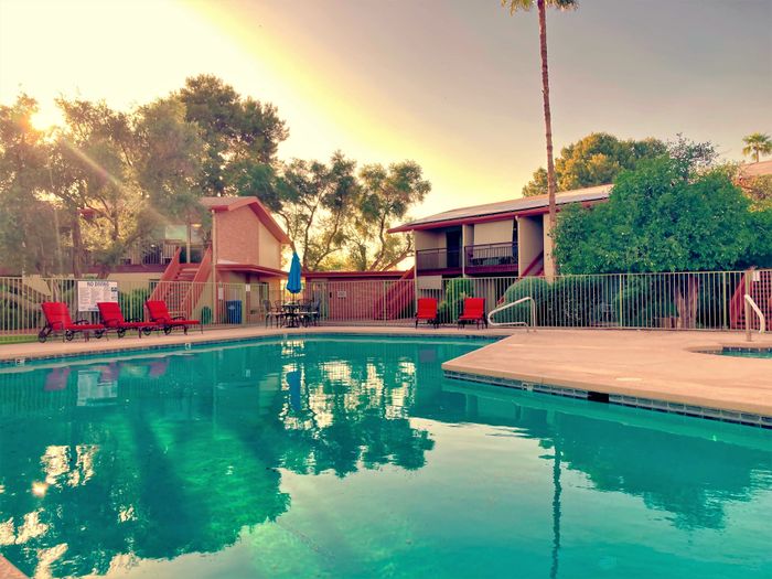 Charming apartment complex with a sparkling swimming pool, surrounded by lush greenery and vibrant red sun loungers, perfect for relaxation.