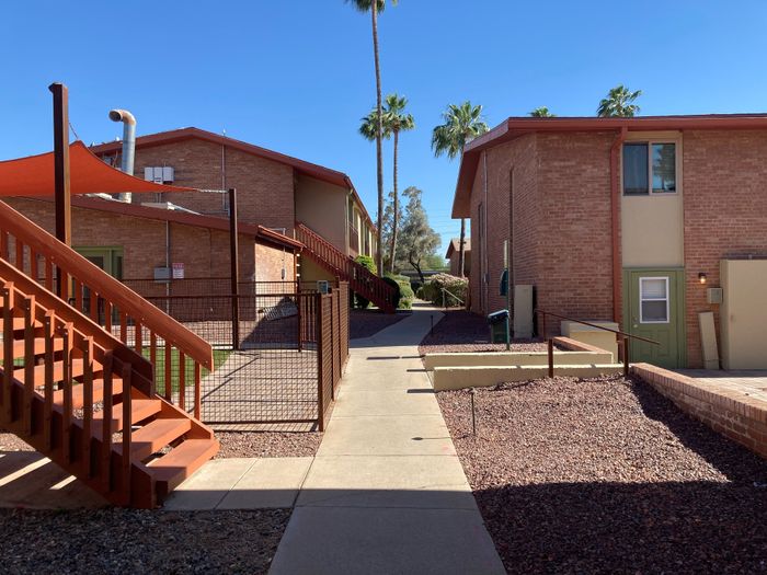 Charming red-brick apartment complex with inviting outdoor walkways, surrounded by lush palm trees under a clear blue sky.