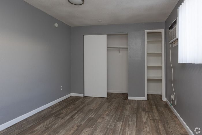 Spacious bedroom with sleek wood flooring, minimalist gray walls, and a functional closet, ideal for modern living.