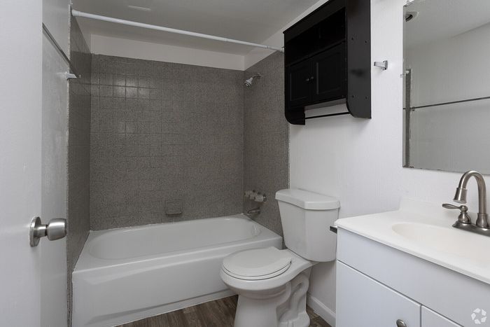 Modern bathroom featuring sleek gray tiles, a pristine bathtub, elegant fixtures, and convenient storage space.