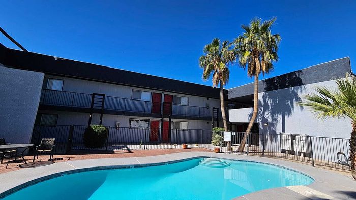 Bright apartment complex with a refreshing pool and lush palm trees, perfect for sun-drenched relaxation.