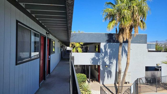 Contemporary apartment exterior with vibrant red doors, lush palm trees, and sleek design under a bright blue sky.
