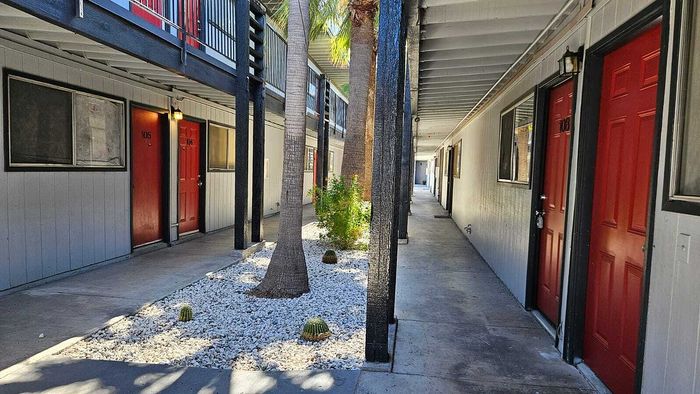 Charming apartment hallway with vibrant red doors, bright natural light, and inviting palm landscaping.