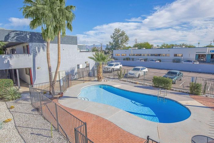 Inviting apartment complex featuring a sparkling outdoor pool with surrounding palm trees and a sunny courtyard.