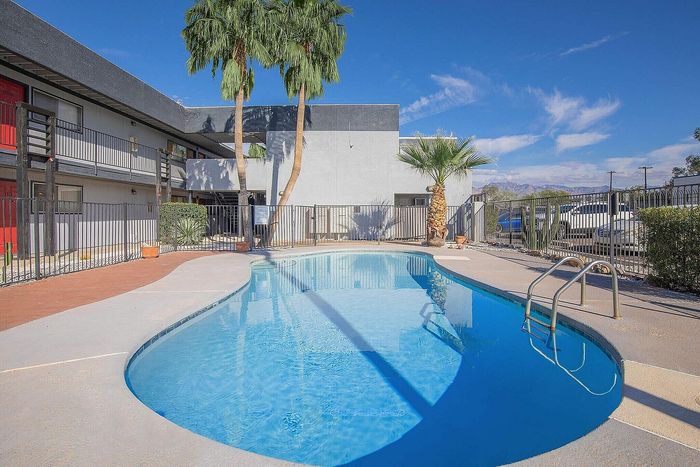 Inviting apartment complex pool area with lush palm trees and a clear blue sky, offering a perfect spot for relaxation and leisure.