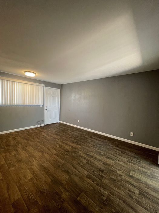 Spacious, light-filled room with elegant wood flooring and modern neutral walls, perfect for a cozy living area.