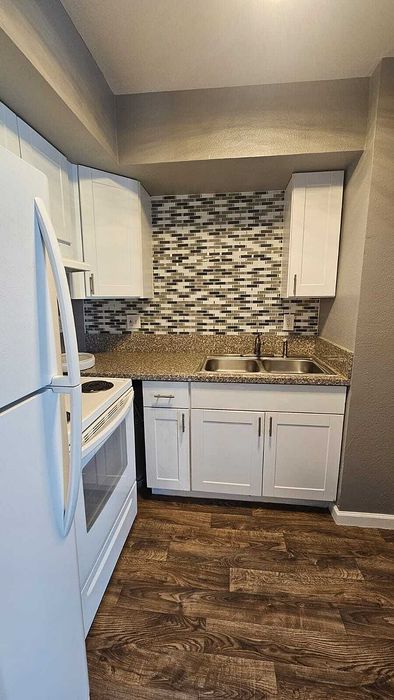Cozy kitchen with sleek white cabinets, modern dual sinks, stylish mosaic backsplash, and elegant wood flooring.