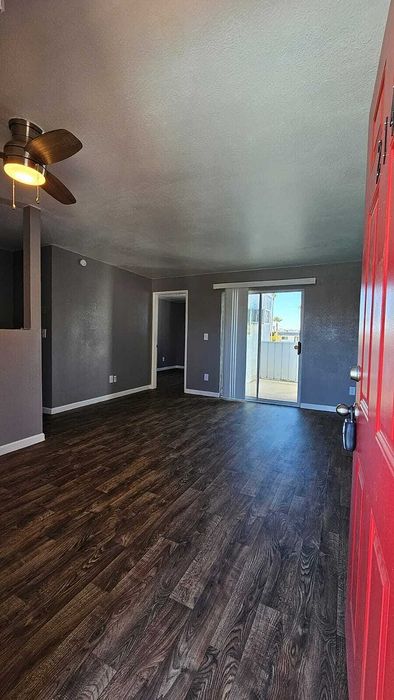 Inviting living room with sleek hardwood floors, modern ceiling fan, and bright glass doors leading to a balcony.
