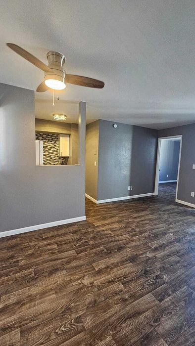Modern open-plan apartment featuring elegant wood flooring, a stylish ceiling fan, and a partially open kitchen with contemporary backsplash.