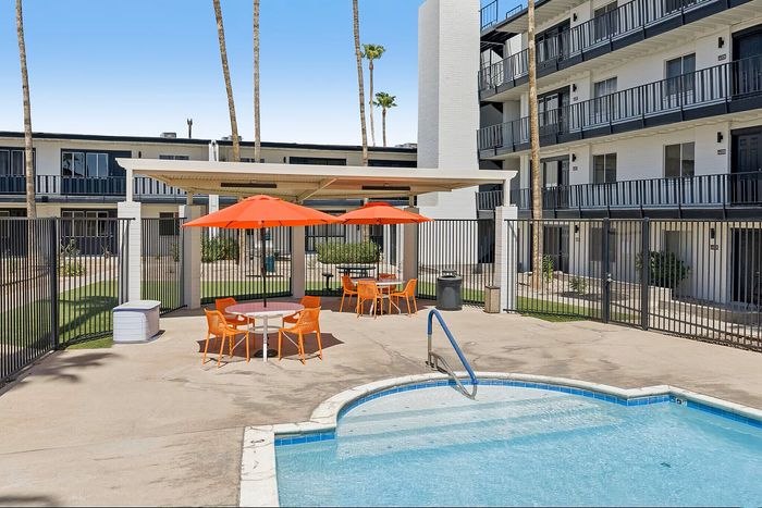 Inviting apartment complex with a refreshing pool area surrounded by vibrant orange seating and shade umbrellas, ideal for relaxation.