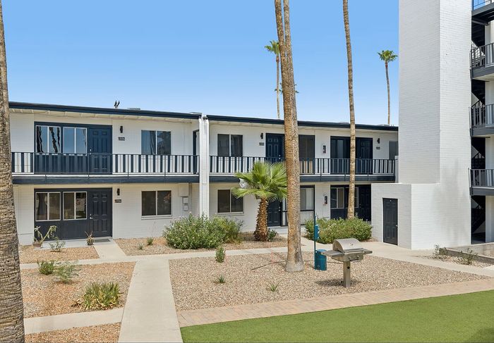 Modern apartment complex with sleek design, featuring lush landscaping and community BBQ area.