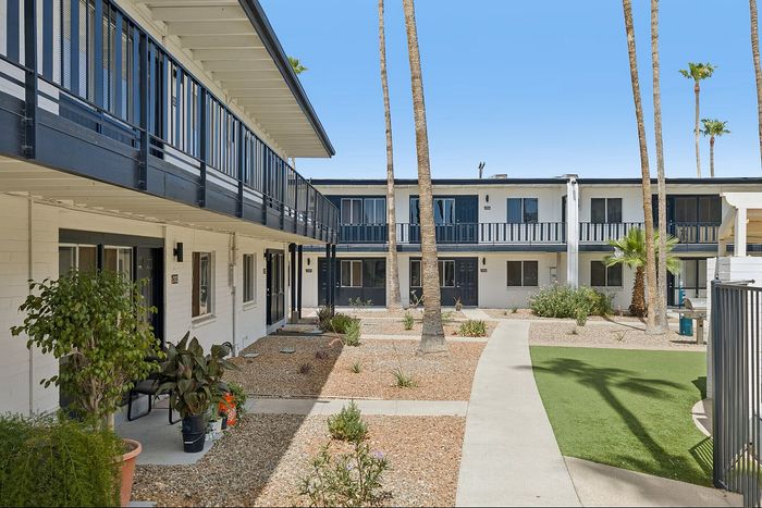 Charming apartment complex with lush landscaping and stylish blue railing, offering a serene courtyard view.